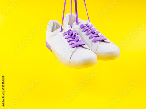 White sneakers with purple laces on yellow background. Modern minimal fashion art trendy bold color still life