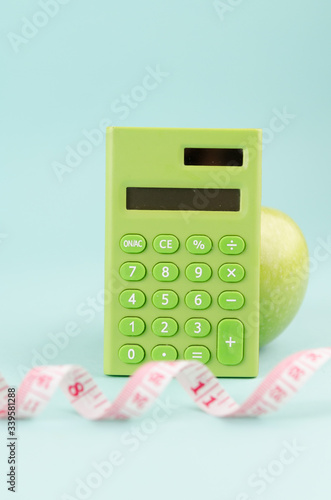 Healthy diet concept with a green calculator, measuring tape and apple