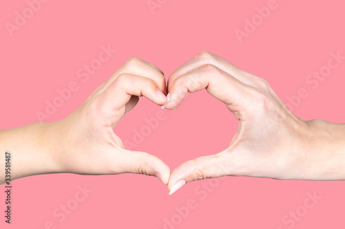 Closeup view of one adult female hand of mother and one small childs hand of son or daughter isolated at pink background. People making heart gesture together as symbol or sign of love and happiness.