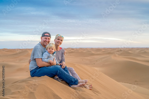 Mother, father and 2 years old boy sitting on top of the sand dune, Sahara Desert