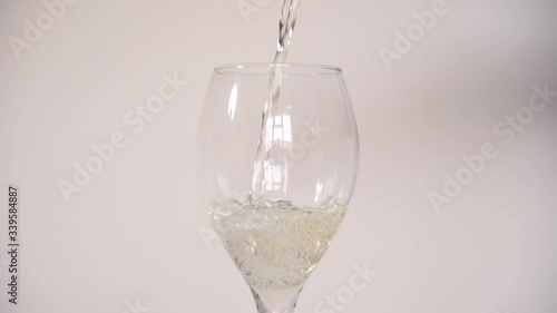 Pouring white wine into an empty tear drop shaped wine glass against a plain white background in slow motion