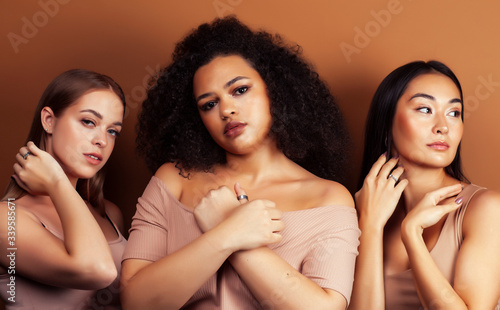 young pretty asian, caucasian, afro woman posing cheerful together on brown background, lifestyle diverse nationality people concept