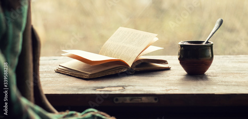 Cup of coffee and an open old book on a wooden windowsill