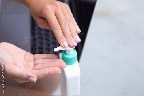 Closeup  woman using hand sanitizer by pumping alcohol gel and washing before working with laptop