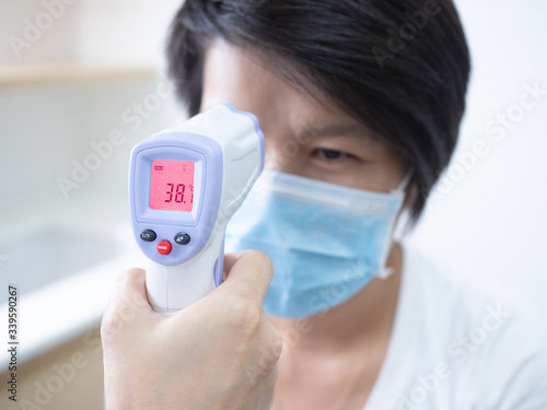 Woman doctor holding medical infrared forehead thermometer checking body temperature of coronavirus infected patients in quarantine area, showing high fever. Covid-19 and coronavirus concept.