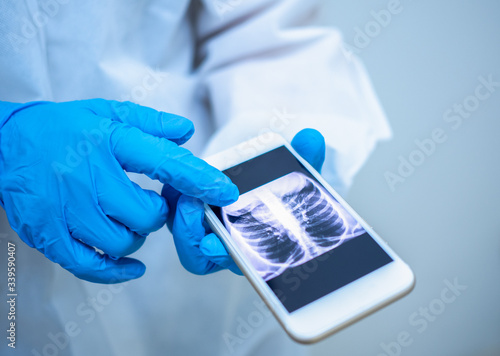 Asian woman doctor in personal protective suit or PPE holding smartphone with chest x-ray film from covid-19 quarantine patient for diagnosis coronavirus infection. Coronavirus, covid-19 concept.