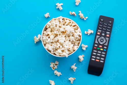 Popcorn and remote control viewed from above on blue background. Flat lay of pop corn bowl. Top view