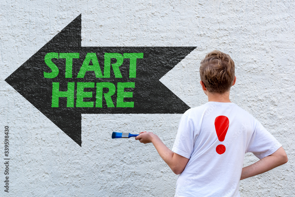 Männlicher Teenager vor einem schwarzen Wegweiser mit dem grünen Text START HERE Männlicher Teenager vor einem schwarzen Wegweiser mit dem grünen Text START HERE