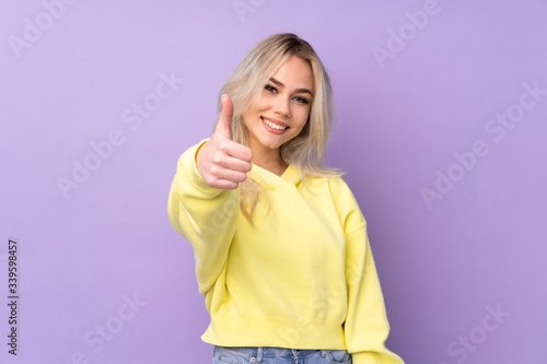 Teenager girl wearing a yellow sweatshirt over isolated purple background with thumbs up because something good has happened