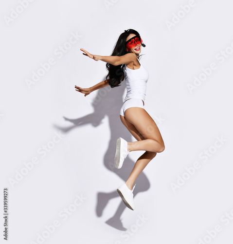 Young beautiful slim brunette woman in sexy white sports clothing or underwear and sunglasses jumping and feeling happy