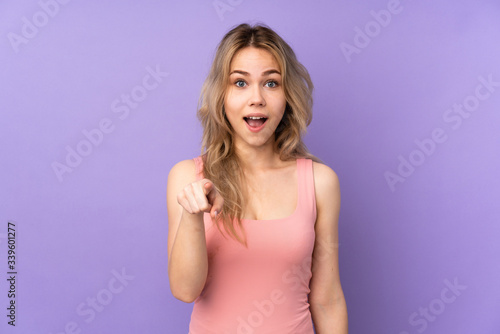 Teenager Russian girl isolated on purple background surprised and pointing front