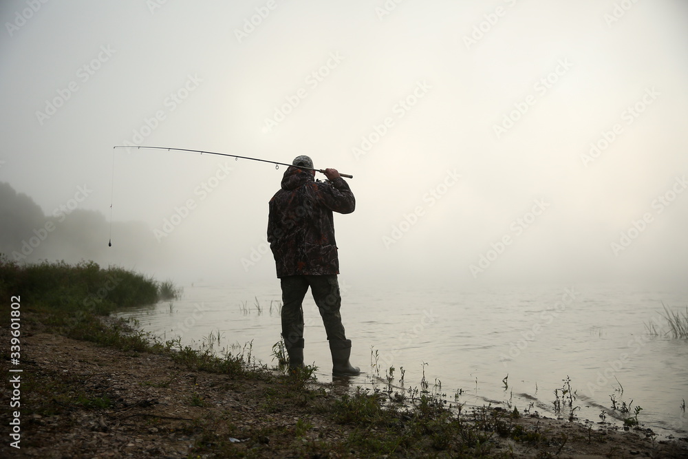 fisherman holding fishing rod on the lake in fog