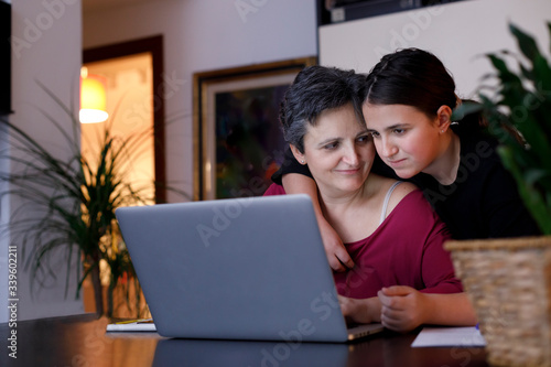 Madre e figlia si abbracciano affettuosamente davanti al computer a casa 