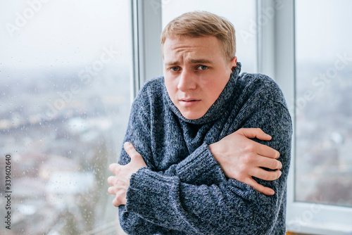 Young man feeling cold in flat near the window photo