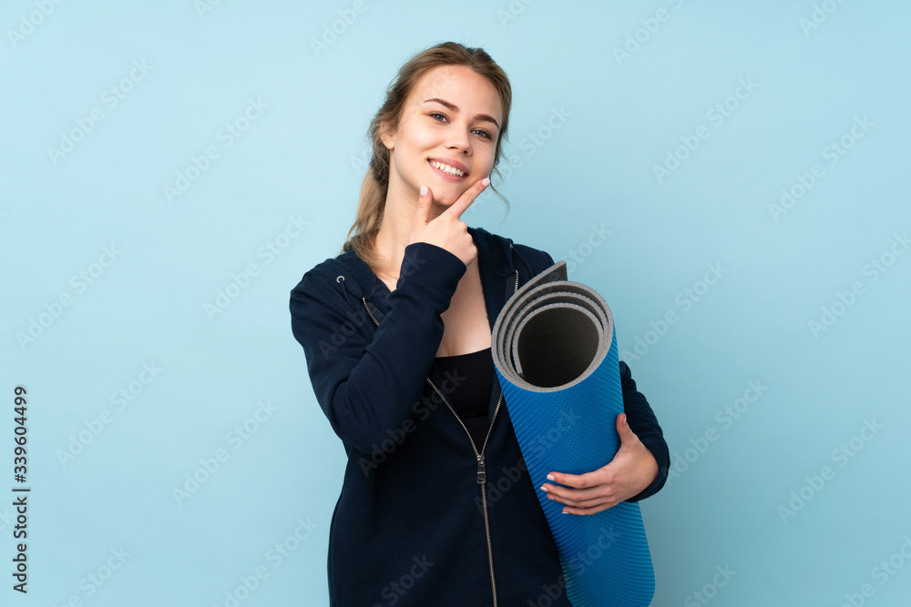 Fototapeta premium Teenager Russian girl holding mat isolated on blue background smiling