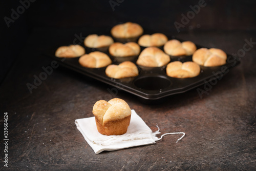 Freshly Baked Homemade Cloverleaf Rolls in Muffin Tin: One Roll on Napkin in Front; Rustic, Dark Background