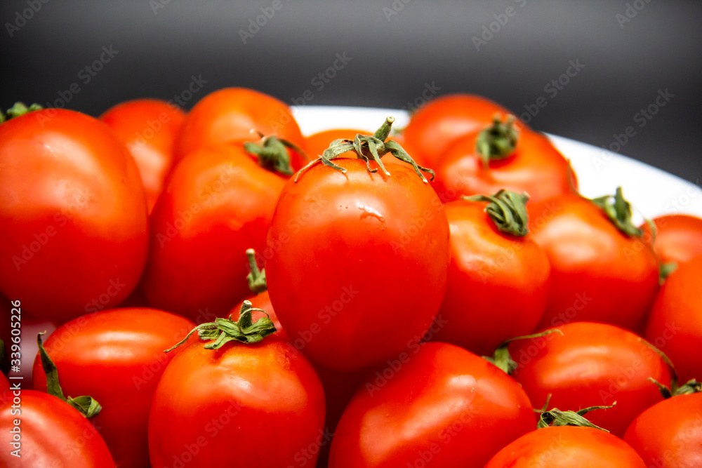Ripe fresh red cherry tomatoes on a white plate against dark background. Beautiful and healthy fresh cherry tomatoes without GMO. Ripe fresh red cherry tomatoes on a white plate against dark background. Beautiful and healthy fresh cherry tomatoes without GMO.