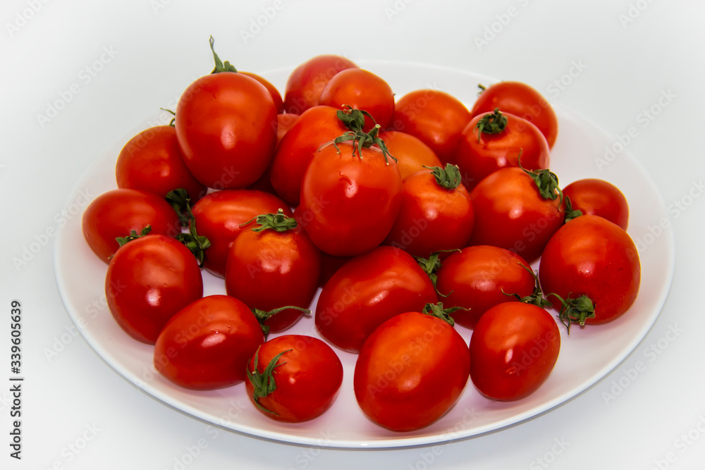 Ripe fresh red cherry tomatoes on a white plate against white background. Beautiful and healthy fresh cherry tomatoes without GMO. Ripe fresh red cherry tomatoes on a white plate against white background. Beautiful and healthy fresh cherry tomatoes without GMO.
