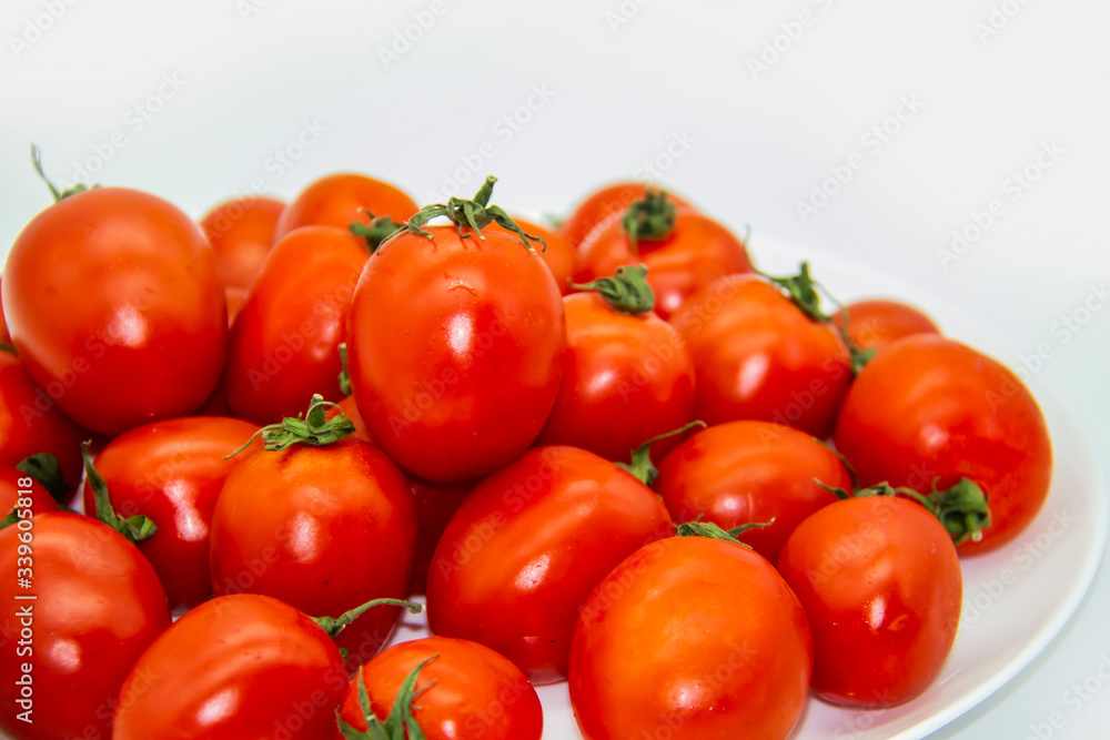 Ripe fresh red cherry tomatoes on a white plate against white background.  Beautiful and healthy fresh cherry tomatoes without GMO.