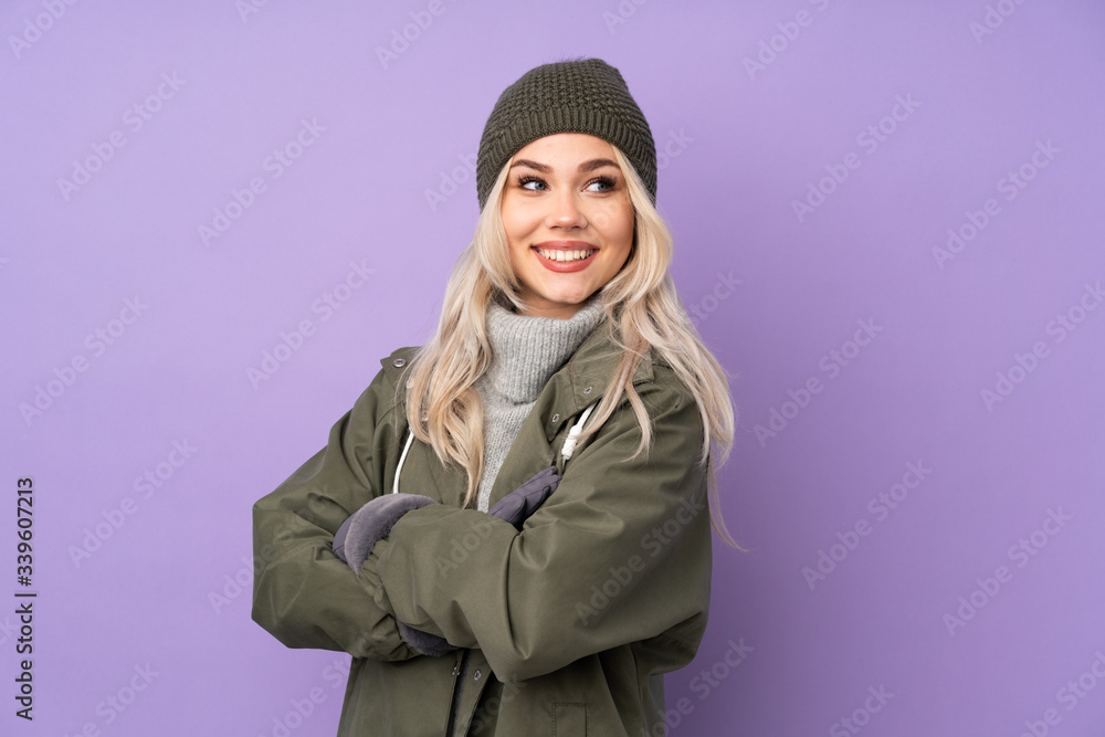 Teenager blonde girl with winter hat over isolated purple background with arms crossed and happy Teenager blonde girl with winter hat over isolated purple background with arms crossed and happy