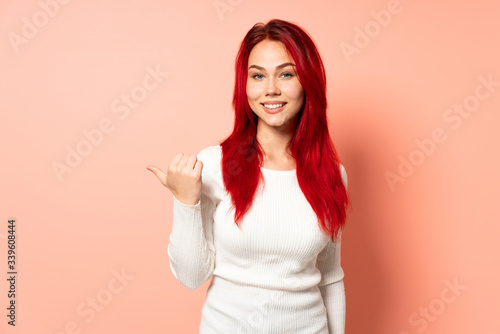 Teenager red hair girl isolated on pink background pointing to the side to present a product © luismolinero