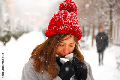 The girl in the red hat covered herself with a scarf. It is snowing in the park.