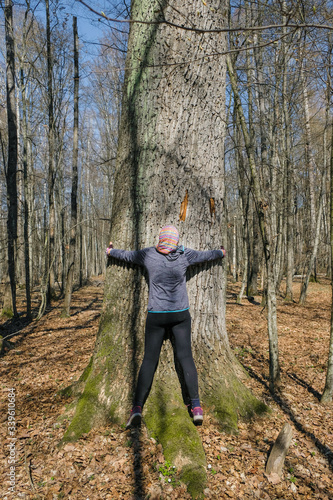 59 year old sporty woman hugging old mighty tree in forest in Ukraine on a sunny day. Back view. © Ganna Zelinska
