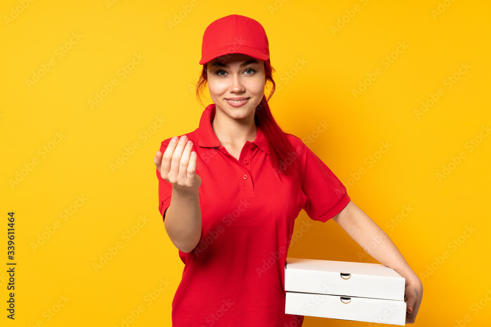 Pizza delivery girl holding a pizza over isolated background inviting to come with hand. Happy that you came Pizza delivery girl holding a pizza over isolated background inviting to come with hand. Happy that you came