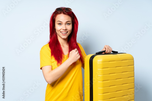 Traveler girl holding a suitcase isolated on blue background celebrating a victory