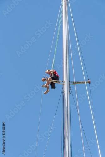 Cape Town, South Africa. 2019. Clipper 70 racing yacht with crew member suspended high up the mast. quayside at Victoria Basin V&A Waterfront, Cape Town,