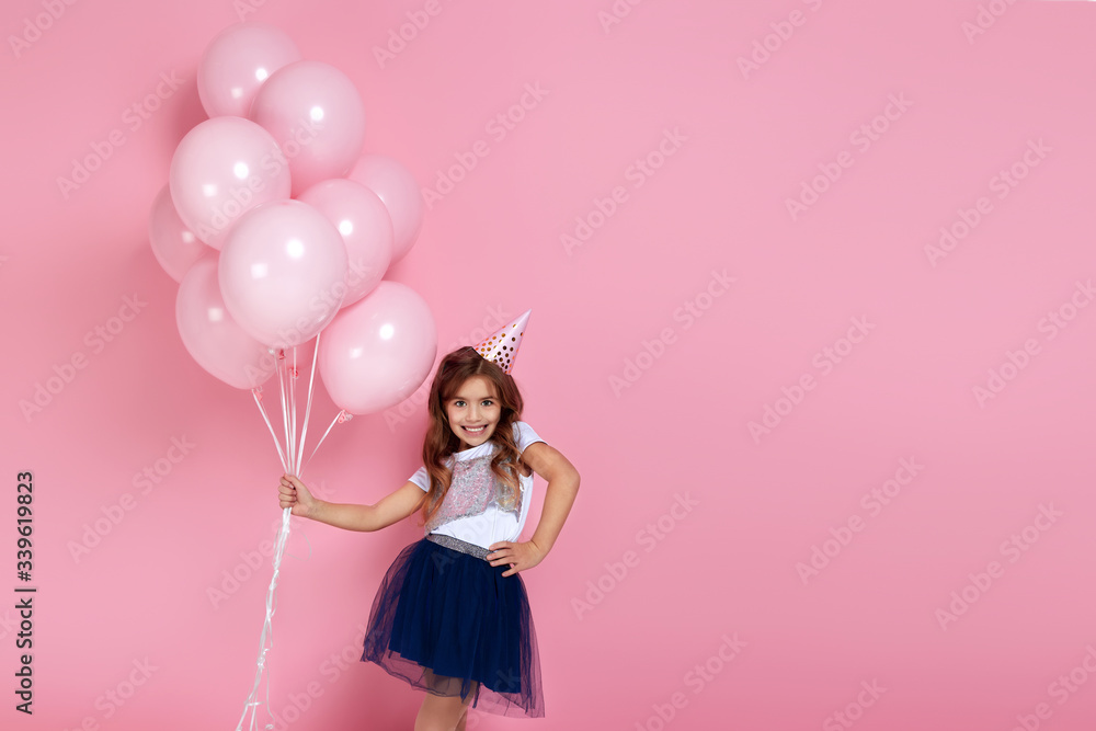 Beautiful happy little child girl in dress and birthday hat posing with pastel pink air balloons isolated on pink background. birthday party. copy space Beautiful happy little child girl in dress and birthday hat posing with pastel pink air balloons isolated on pink background. birthday party. copy space