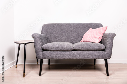 A cute gray settee with a pink pillow sitting on it, next to a small, contemporary occasional table. 