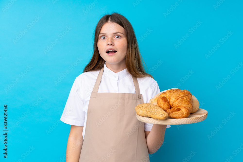 Ukrainian teenager chef uniform. Female baker holding a table with several breads with surprise and shocked facial expression Ukrainian teenager chef uniform. Female baker holding a table with several breads with surprise and shocked facial expression