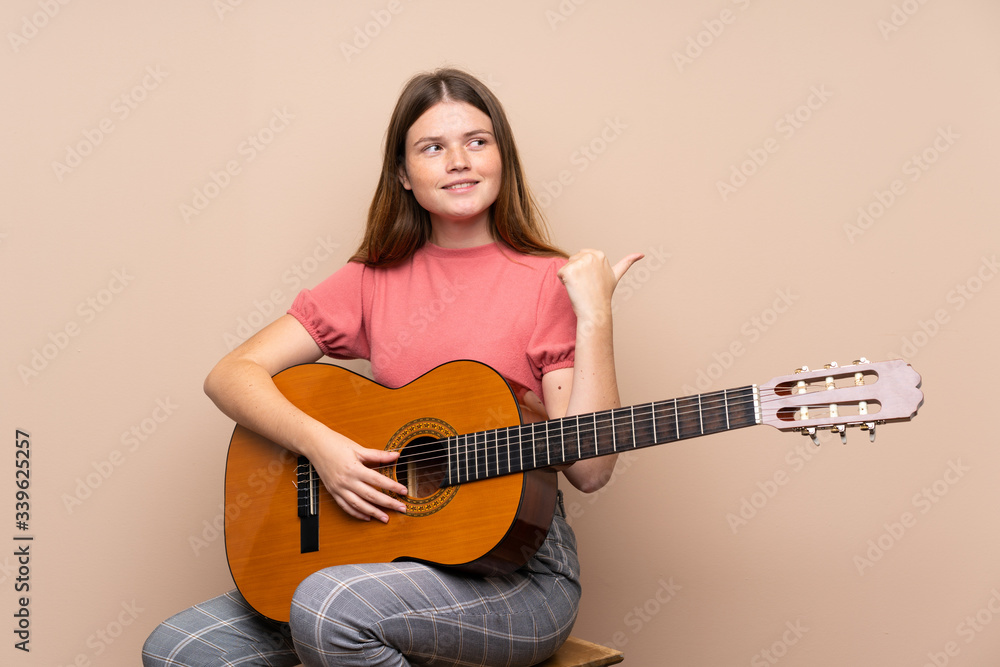Ukrainian teenager girl with guitar over isolated background pointing to the side to present a product Ukrainian teenager girl with guitar over isolated background pointing to the side to present a product