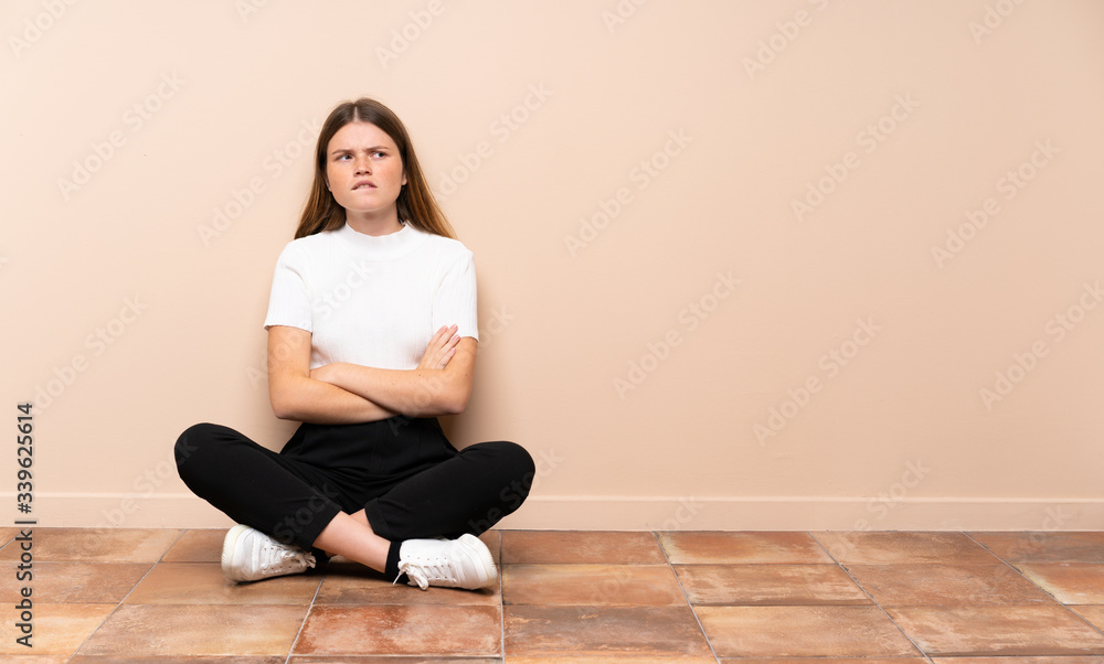 Ukrainian teenager girl sitting on the floor with confuse face expression