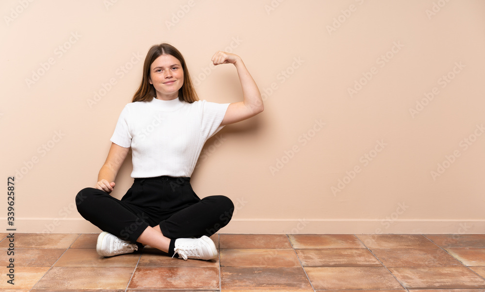 Ukrainian teenager girl sitting on the floor doing strong gesture Ukrainian teenager girl sitting on the floor doing strong gesture