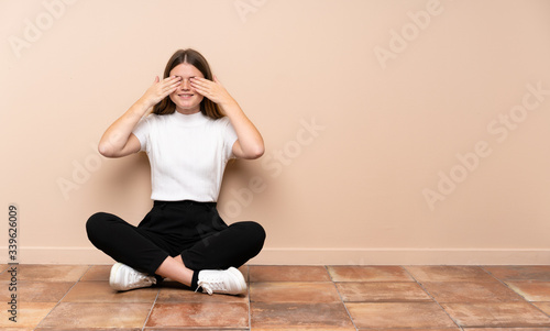 Ukrainian teenager girl sitting on the floor covering eyes by hands