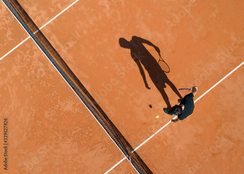 Long shadow of a tennis player on a tennis earthen ground