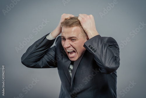Half-length portrait of businessman putting hands on head and shouting. Concept of shock, headache and high temperature