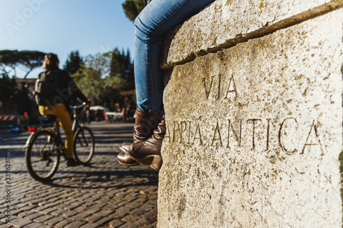 pretty woman legs sitting on the via appia antica. Cyclist in the background. Interesting place tourist guide rome italy