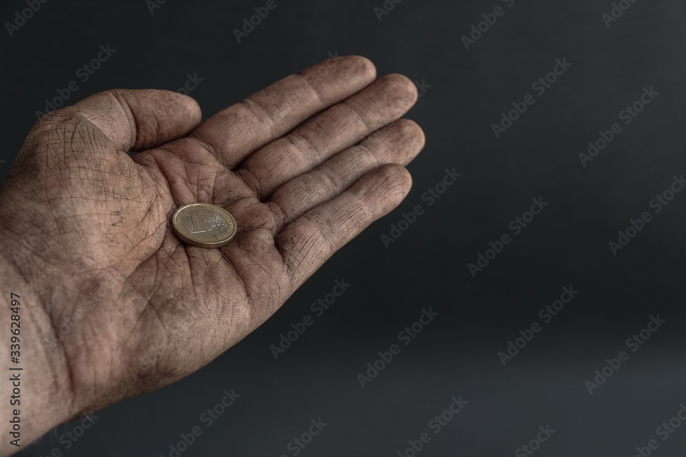 One euro coin lies in dirty begging hand of unemployed man on the dark background. Theme of job loss during the economic crisis. Copy space. One euro coin lies in dirty begging hand of unemployed man on the dark background. Theme of job loss during the economic crisis. Copy space.