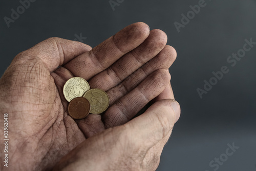 A fiew euro cent coins lies in dirty cupped hands of homeless man on the dark background. Theme of the onset of the economic crisis. photo