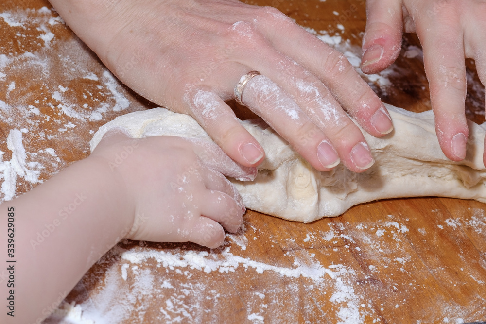 Hands of mother and little daughter knead the dough on a wooden table. The concept of family cooking baking bringing together parents and children.