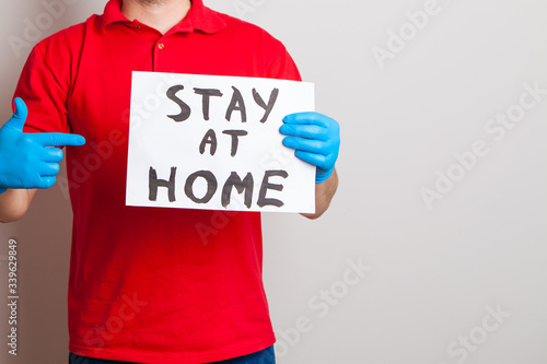 stay at home. A man in a red T-shirt with gloves and a medical mask holds a tablet in his hands. on a white background