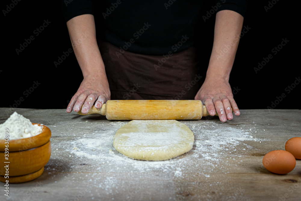 Man hands kneading bread dough on a wooden table with black background Man hands kneading bread dough on a wooden table with black background