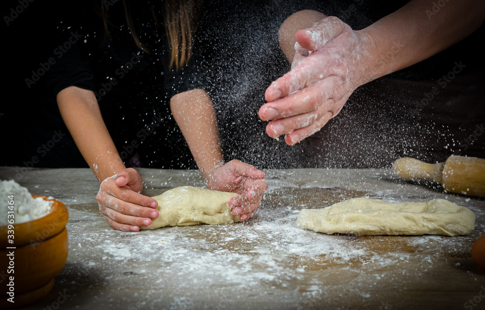 Hands of man and girl kneading bread dough on a wooden table with black background Hands of man and girl kneading bread dough on a wooden table with black background