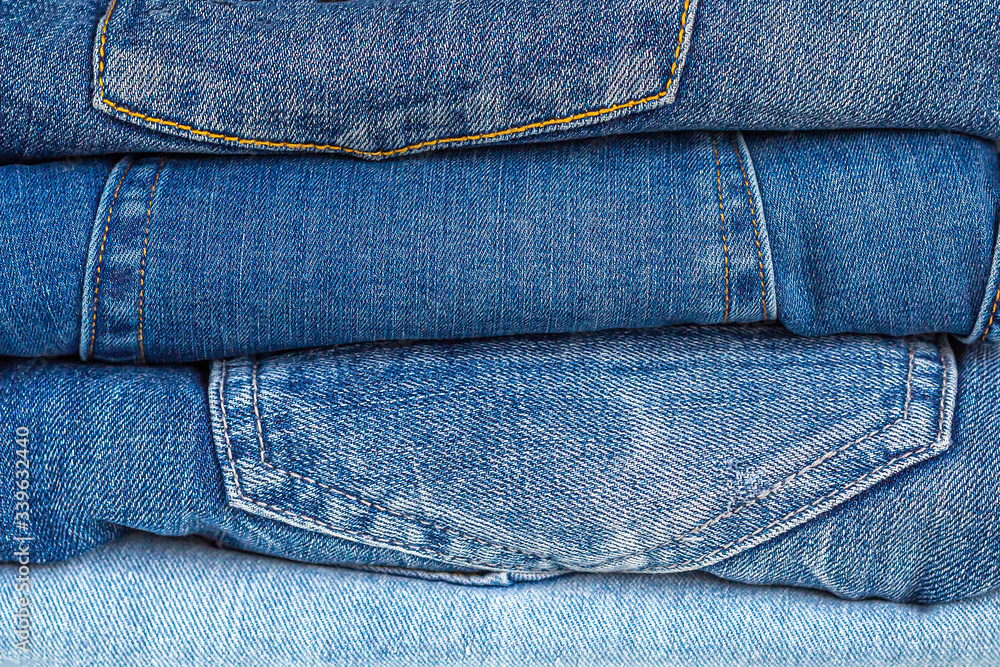 Denim background. Neat stack of various shades of blue jeans. Clothes storage. Denim background. Neat stack of various shades of blue jeans. Clothes storage.