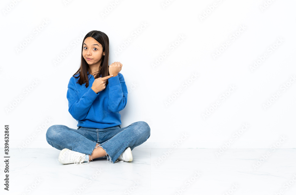 Young mixed race woman sitting on the floor isolated on white background making the gesture of being late Young mixed race woman sitting on the floor isolated on white background making the gesture of being late