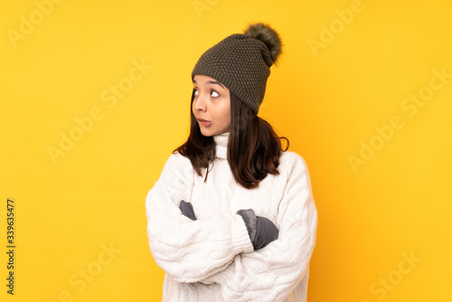 Young woman with winter hat over isolated yellow background with confuse face expression © luismolinero