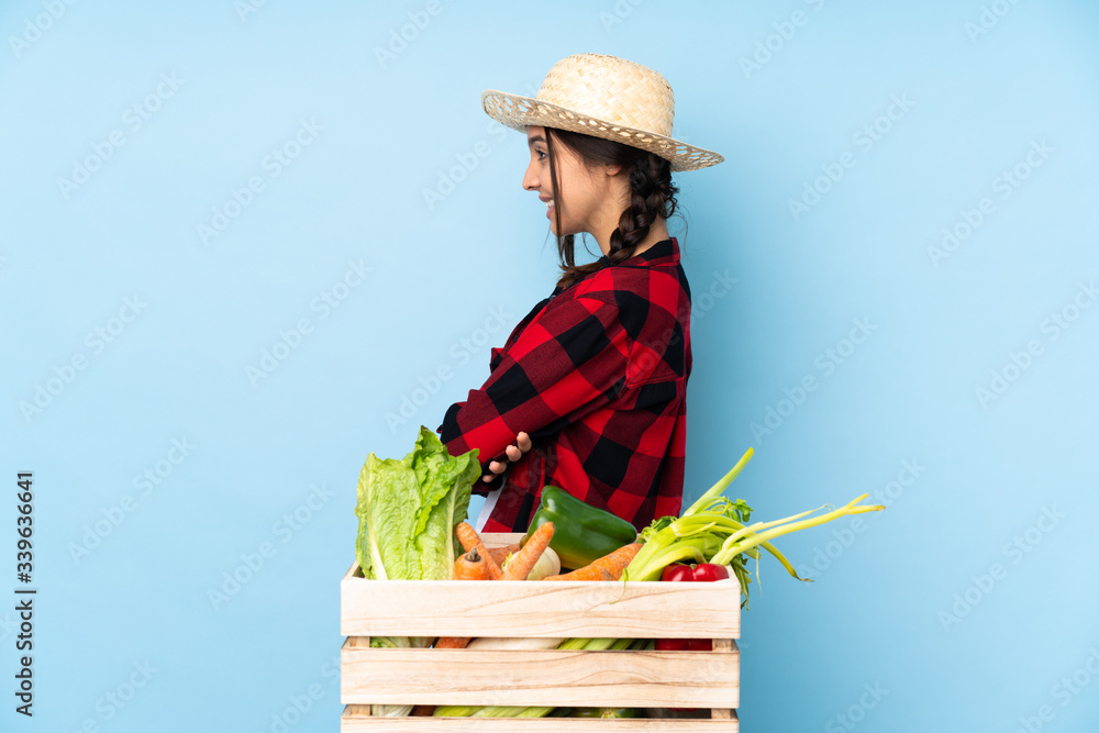 Young farmer Woman holding fresh vegetables in a wooden basket in lateral position